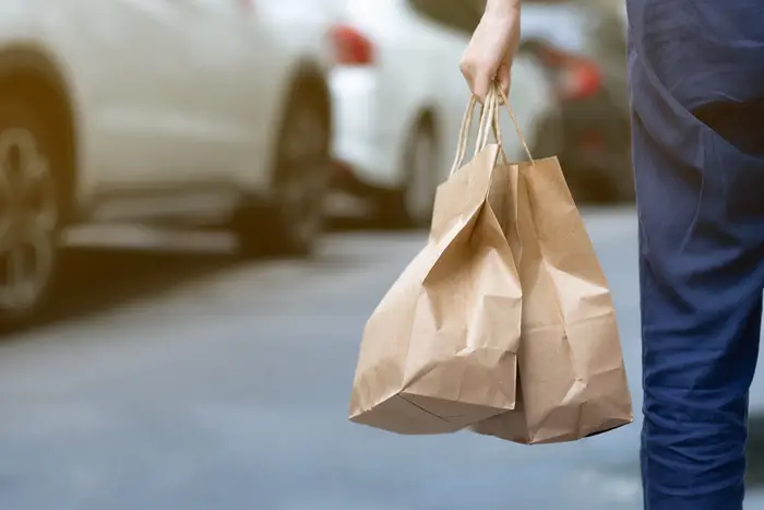 A person is holding two brown paper bags containing a takeout food order.